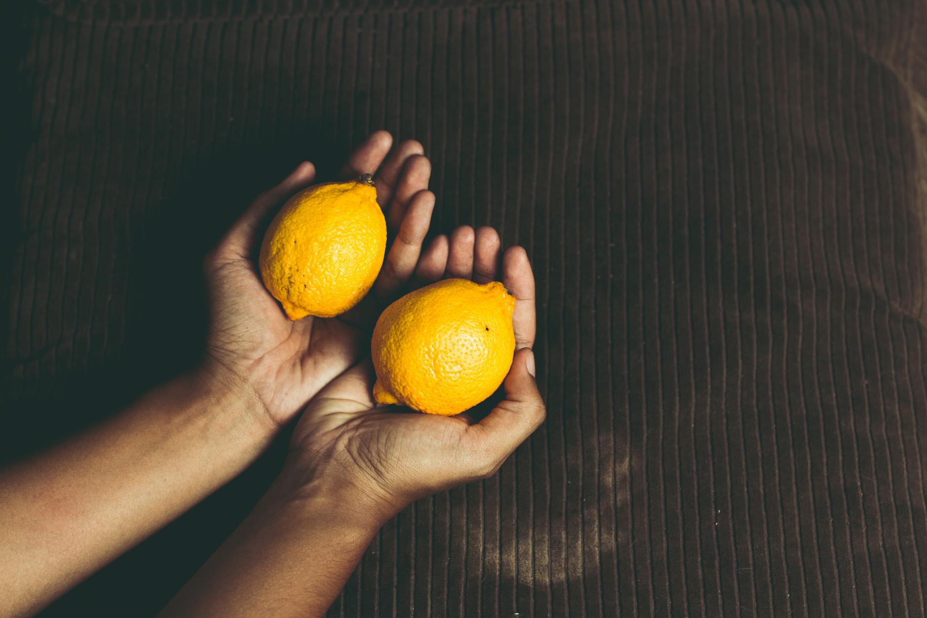 A close-up of a hand holding an orange vibrator against a minimalistic purple backdrop