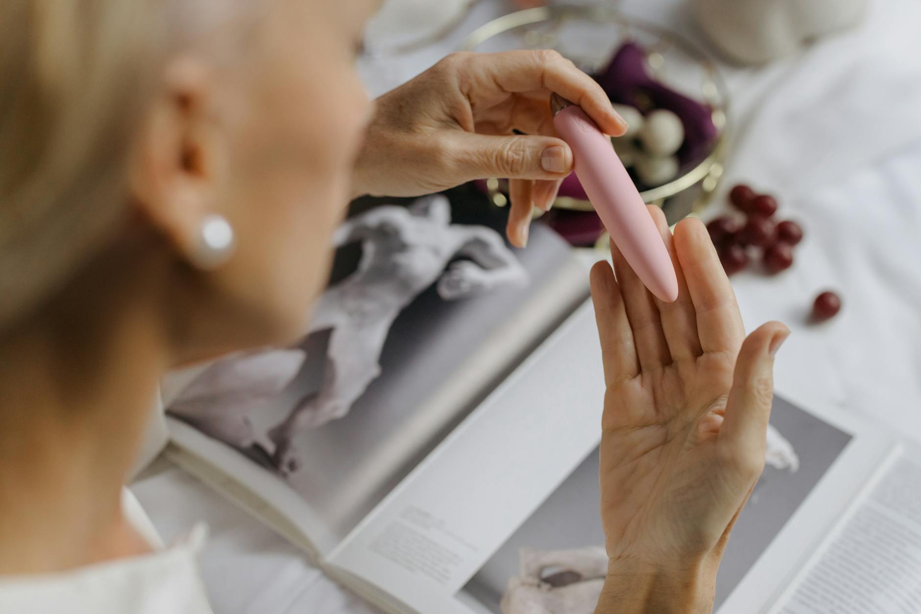 Hand hält rosa Vibrator mit Kunstbüchern im Hintergrund, betont intime Themen