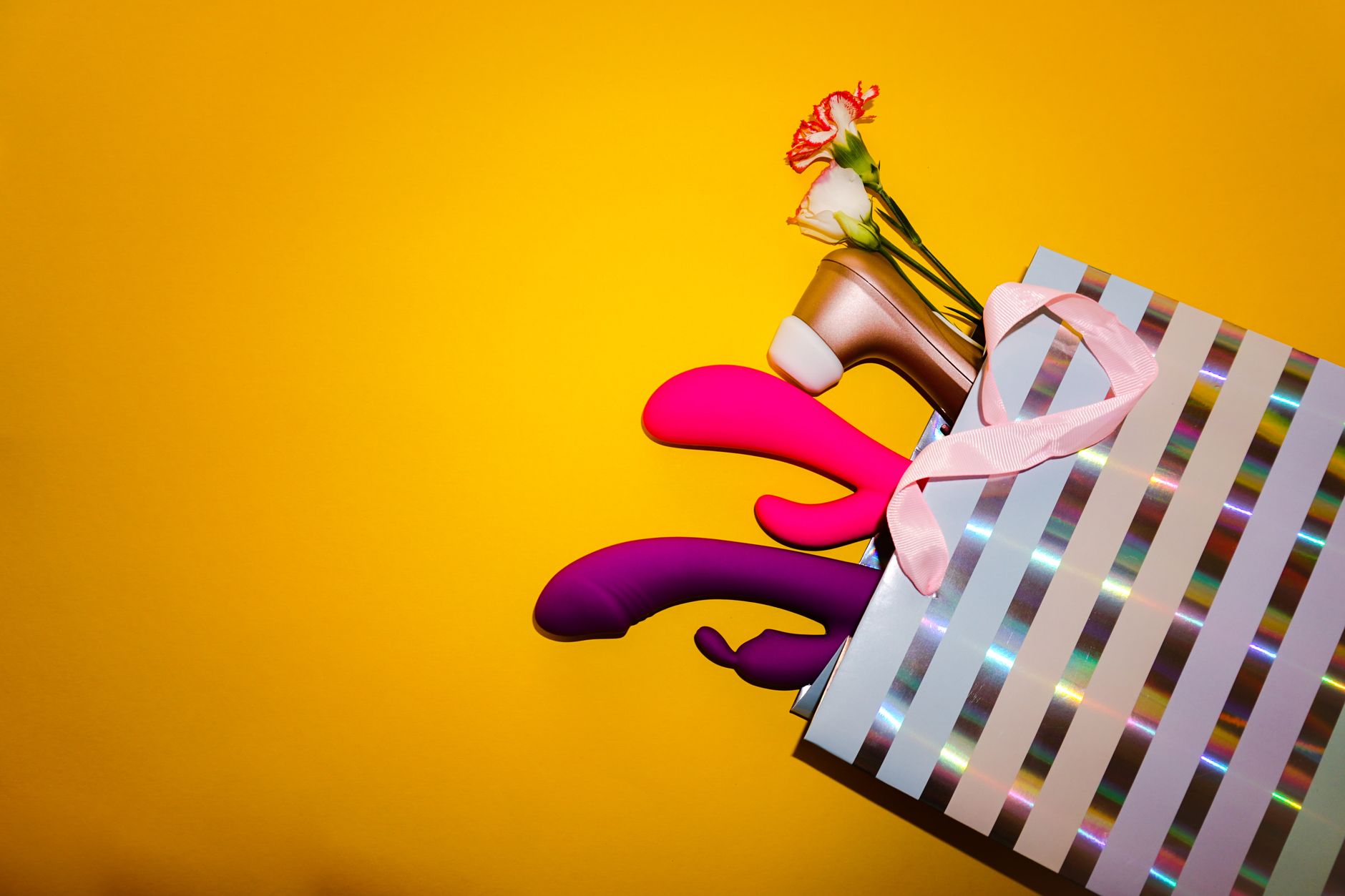 Farbenfrohe Vibratoren in einer Geschenktüte mit Blumen auf gelbem Hintergrund