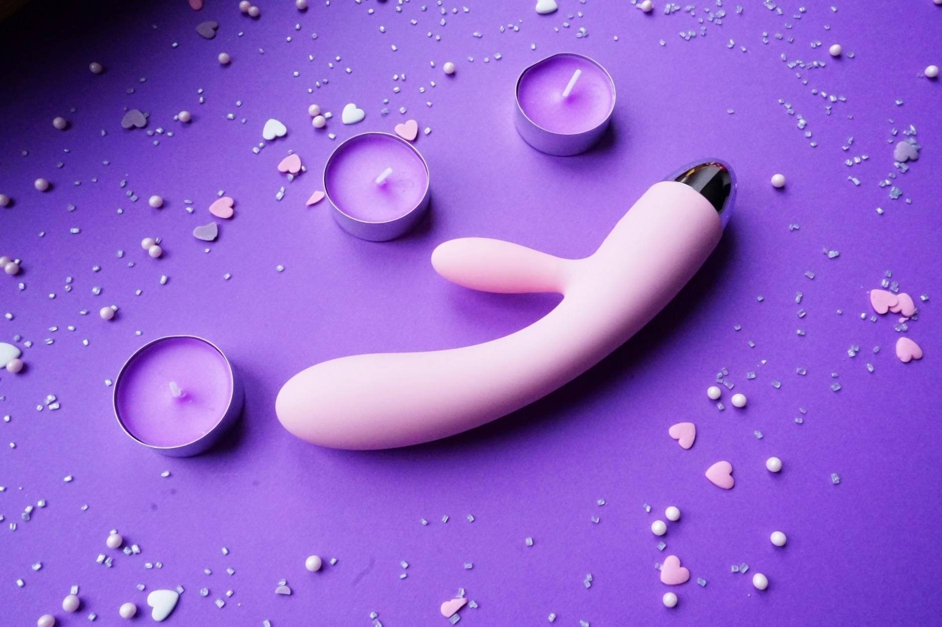 Pink vibrator on purple background with heart confetti and candles in romantic setting